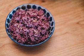 A blue and white ceramic bowl filled with purple rice, on a wood surface