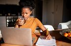Person drinking a glass of water while looking at a computer and taking notes.