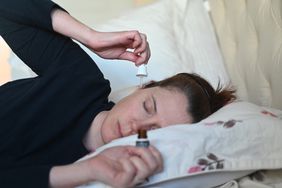 Person laying on their side in bed and putting in ear drops.