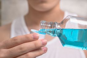 Man pouring light blue mouthwash into a cap.
