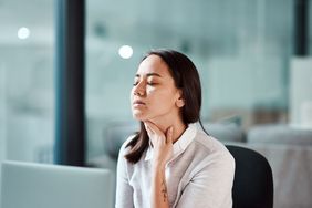 person with an itchy neck scratching it while sitting on desk