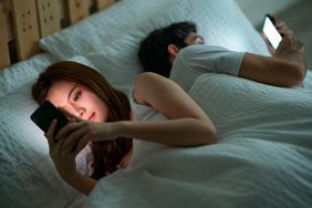 young couple using their cellphones in bed at morning back to back