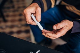 Senior man checking his blood sugar, on a daily basis while using a glucometer so he can know how many doses of insulin he needs to give himself.