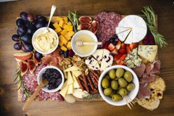 Overhead image of a charcuterie board: cheeses, meats, dips, grapes, figs, berries, apples, olives, and rosemary sprigs.