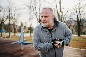 older man wearing workout clothes and headphones experiencing chest pain while exercising in the park