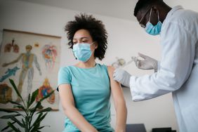 Person with mask on gets a COVID vaccine from doctor with mask on in office.
