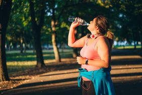 Woman drinking water while running in a park.