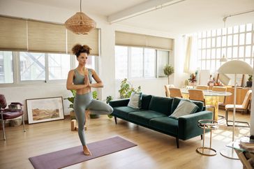 person practicing a tree pose on a yoga mat in a bright living room
