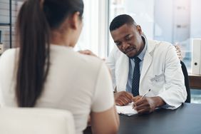 A doctor and a patient sit at a desk for a medical consultation. 