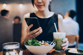 woman eating salad looking at phone