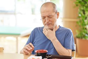 A man holds a hand to his throat in discomfort while swallowing food
