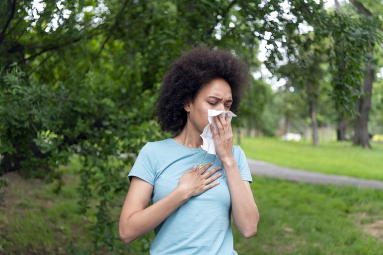 Person coughs into a tissue outside and holds their chest.