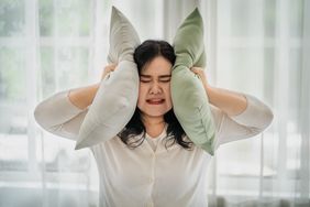 person covering her ears with two large pillows to reduce sensory overload