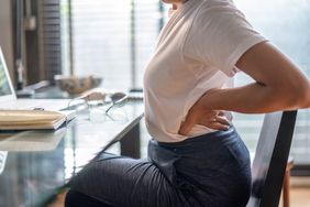 Woman in home office suffering from back pain sitting at computer desk