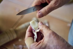 Hands holding and cutting a garlic clove with a knife.