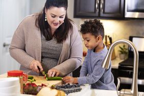mother with obesity cutting vegetables with son in their kitchen