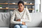 Person sitting on a couch holding their lower stomach in pain.