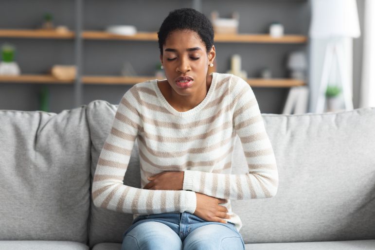 Person sitting on a couch holding their lower stomach in pain.