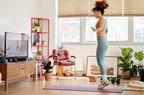 Full length of young woman jumping while exercising at home. Woman is watching online yoga class. She is in living room.