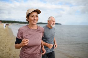 Active senior woman and man running along beach.