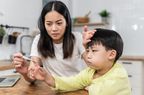 Portrait of Asian mother checking her sick sons temperature, looking at thermometer and touching forehead of her son.