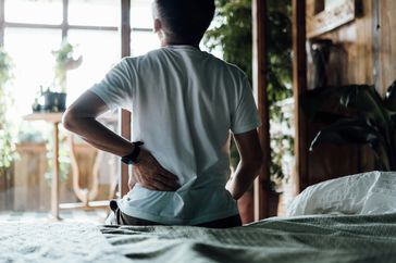 man with pinched nerve in lower back holds back while sitting down
