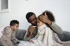 Father checks temperature of daughter in his lap while son looks on.