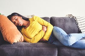Person lying on the couch holding their stomach in pain.