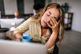 A tired woman has her eyes closed as she sits at a computer