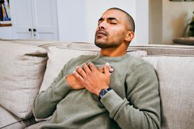 young man sitting on a couch and holding onto chest with both hands due to heart palpitations