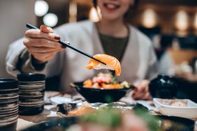 Person eating fresh salmon with chopsticks. 