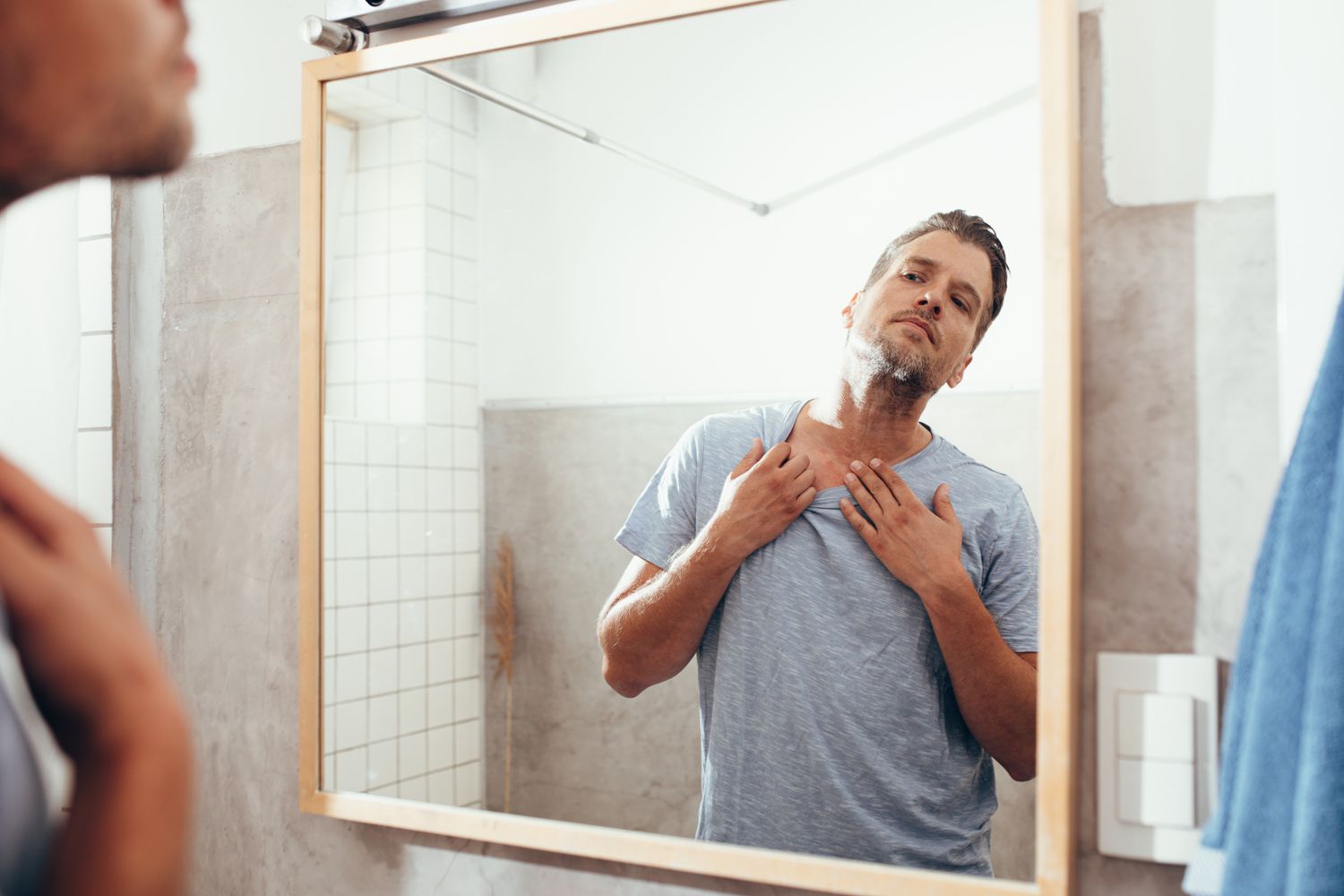 A man inspects his neck in the mirror
