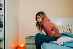 Person holds stomach in discomfort on their bed next to their dog.