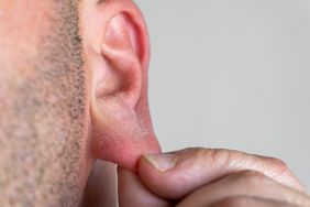 A close-up of a person pulling on their earlobe