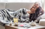 A woman lies on the couch, under a blanket, with a hand over her head