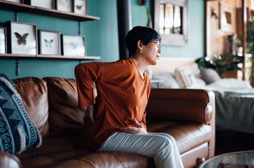 woman sitting on couch suffering from backache