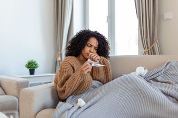 Woman on couch looking at a thermometer. 