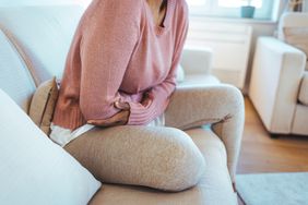 A woman holds her arms over her abdomen in pain