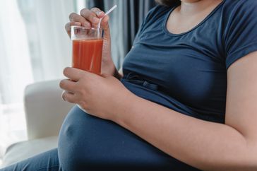 Pregnant person with outie belly button drinking juice