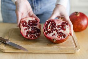 woman's hands holding a halved pomegranate open, the seeds are visible
