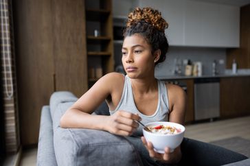 Woman looks out the window while eating a bowl of yogurt. 