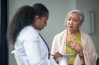 A senior woman shares her chest pain symptoms with her doctor at an appointment. The woman is dressed casually and holding her chest with her hand as she looks downward with a distraught expression. The doctor is sitting in front of her listening attentively.