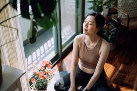 A woman sits, relaxed with her eyes closed next to a window with sun coming in