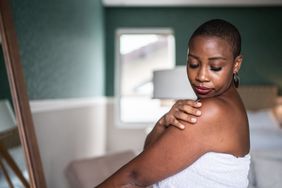 Woman wearing a towel applying moisturizer.