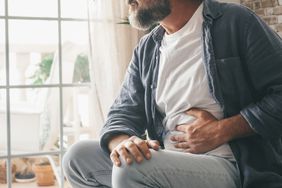 man looking out window holding abdomen in pain