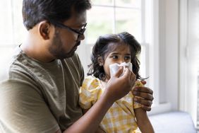 A father helps his daughter blow her nose
