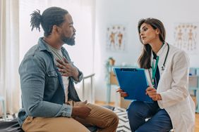 person sitting inside doctor's office holding chest in pain while doctor observes