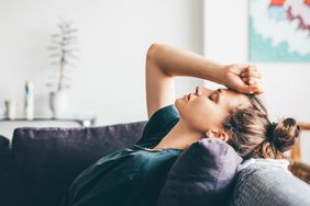 A woman lies on a couch with her eyes closed and her hand to her head