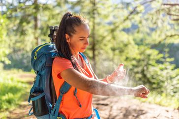 A woman applies mosquito spray during a hike