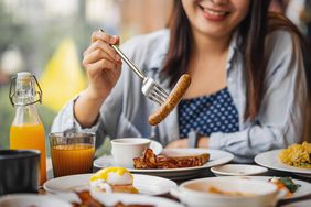 Woman eating sausage at a breakfast table